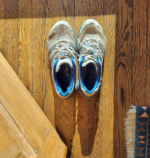 Pair of worn tennis shoes at the threshold of an open door with a shadow cast behind them