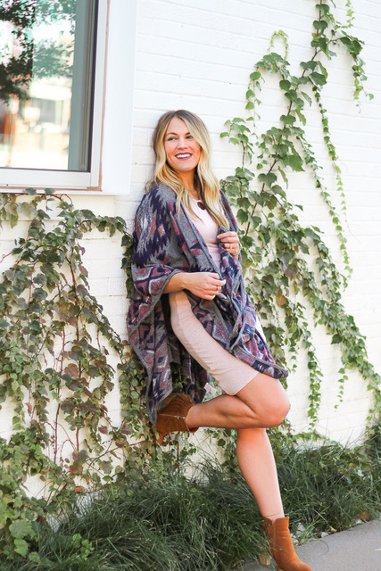 girl leaning against ivy wall wrapped in poncho