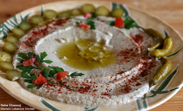 Baba Ghanouj in a serving dish garnished with pickles, tomatoes, parsley