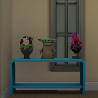 Screenshot from Sims4 game of a table with vase of roses, space rock, and licensed ornament of Baby Yoda named The Child Statue