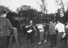 A photograph of a crowd of men outside, some running.