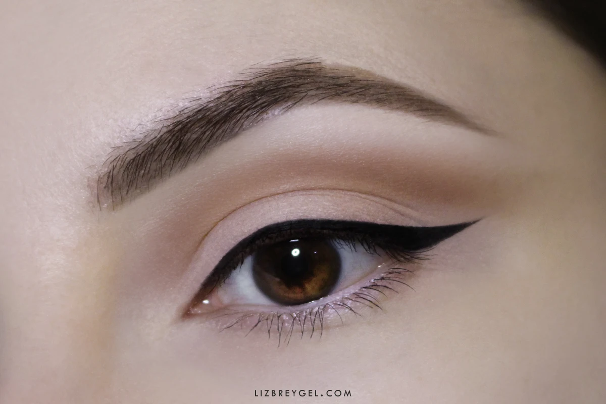 a close-up of a brown hooded eye with a matte everyday makeup look, black eyeliner wing and a highlighter in the inner corner of an eye
