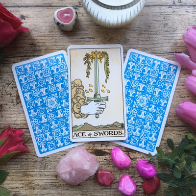 Three blue-backed tarot cards surrounded by pink crystals and flowers