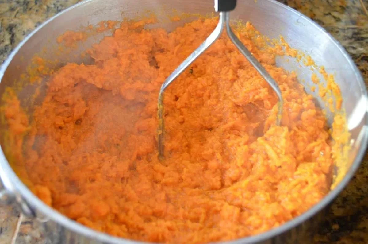 Yams being mashed in a medium sized stainless steel pot.