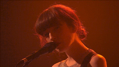 in a red-ish haze environment, a girl is singing looking at us then she looks down