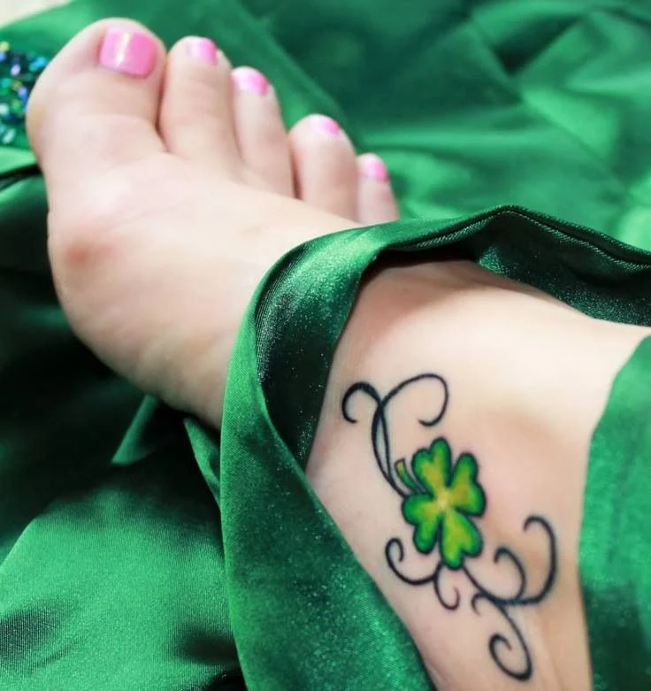 pie de chica envuelto en sedas verdes, lleva tatuaje de trebol en el empeine