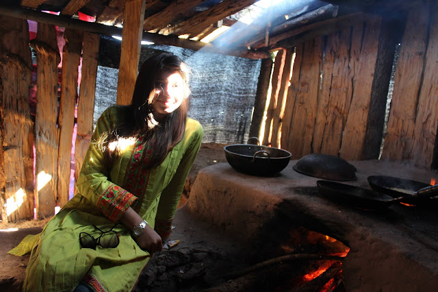 A Beautiful Girl Sitting By A Wooden Stove, In a Wooden Shed, Wearing A Green Dress While The Sun Tries To Catch A Glimpse Of Her.