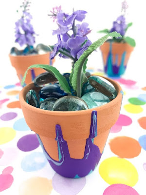 Terracotta flowerpot painted with purple and teal paint poured over it