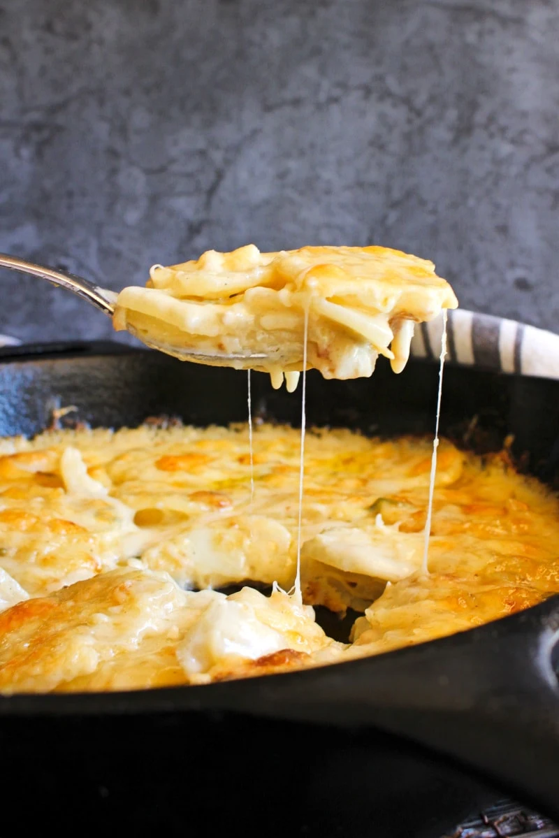 A spoonful of One Skillet Potatoes au Gratin being lifted out of a cast iron skillet.