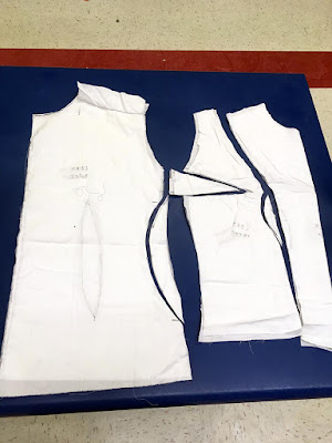 A series of bodice pieces in white muslin laid out on a blue table, with the darts cut free and set back in place for dramatic effect.