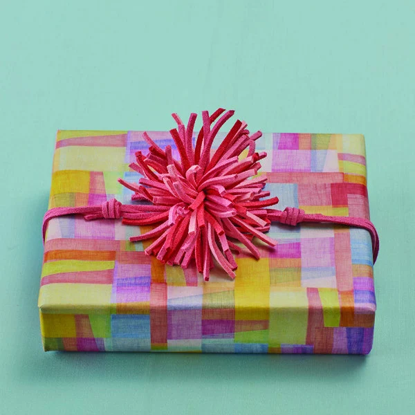 colorfully wrapped, rectangular gift with pink rawhide leather pom pom bow