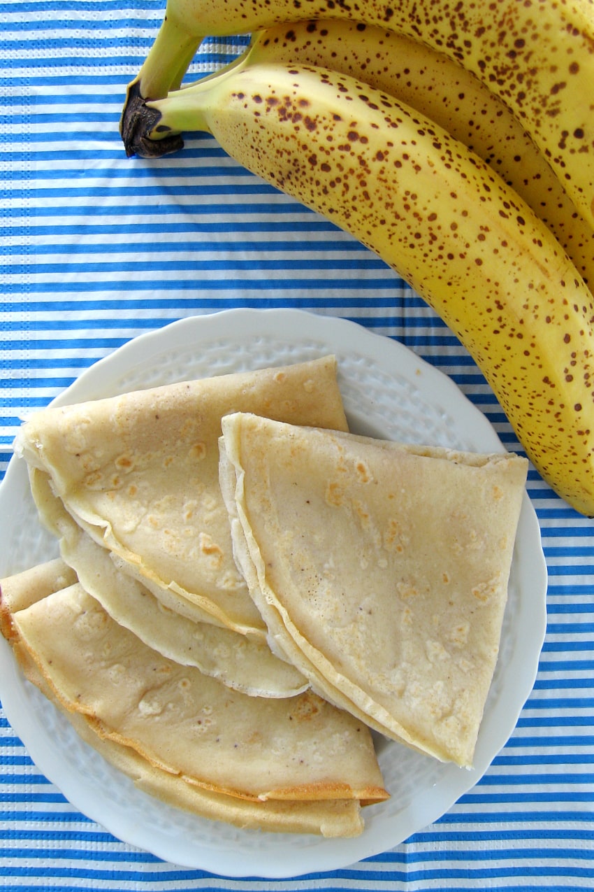 Banana crepes on a plate with fresh unpeeled bananas on the side