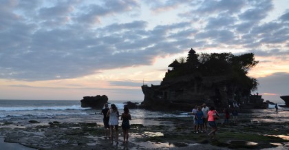 A couple enjoying the sunset at Tanah Lot Temple in Bali. This holy shrine is perched on a cliff overlooking the ocean. The temple is silhouetted against the sky and the sunset is absolutely stunning. They are clearly enjoying this special moment together.