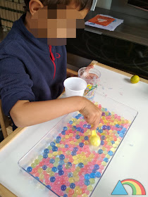 Niño haciendo trasvases de bolas de gel o water beads de colores con vasos y cucharas