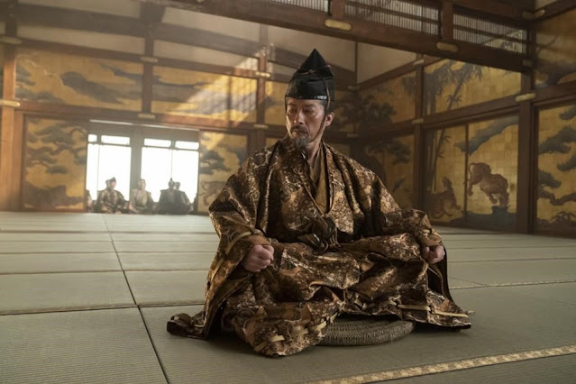 A man dressed in fine Japanese robe sits on ground