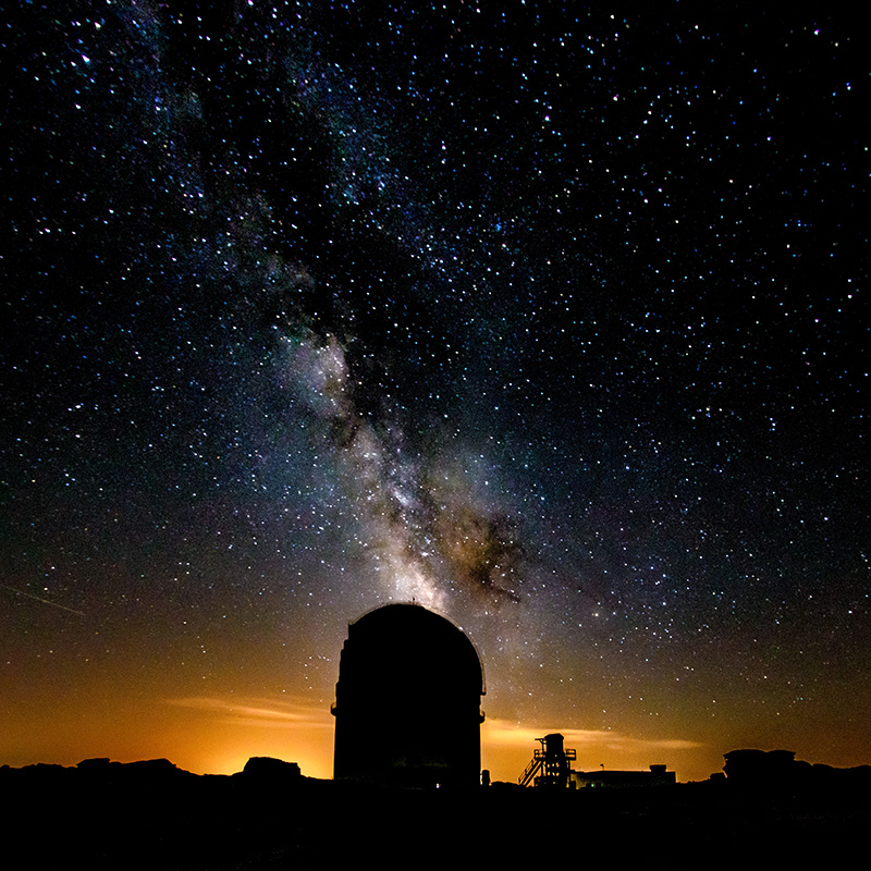 Telescopio del observatorio a contraluz con la Vía Láctea cayendo sobre el horizonte.