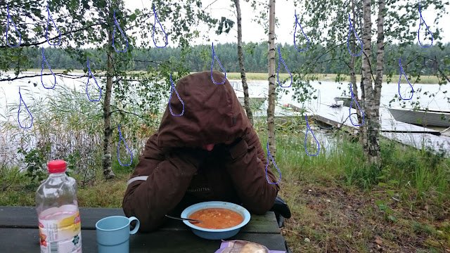 Henkilö istuu huppu päässä ruokapöydässä ulkona