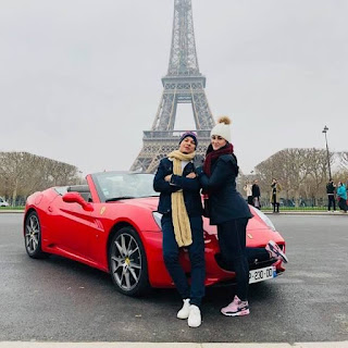 imagem contem um casal encostado a uma ferrari tendo como plano de fundo a Torre Eiffel