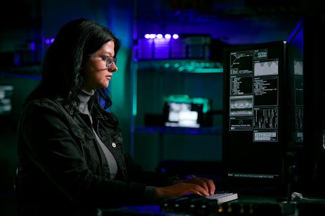 cybersecurity woman wearing glasses with many computers and monitors surrounding her