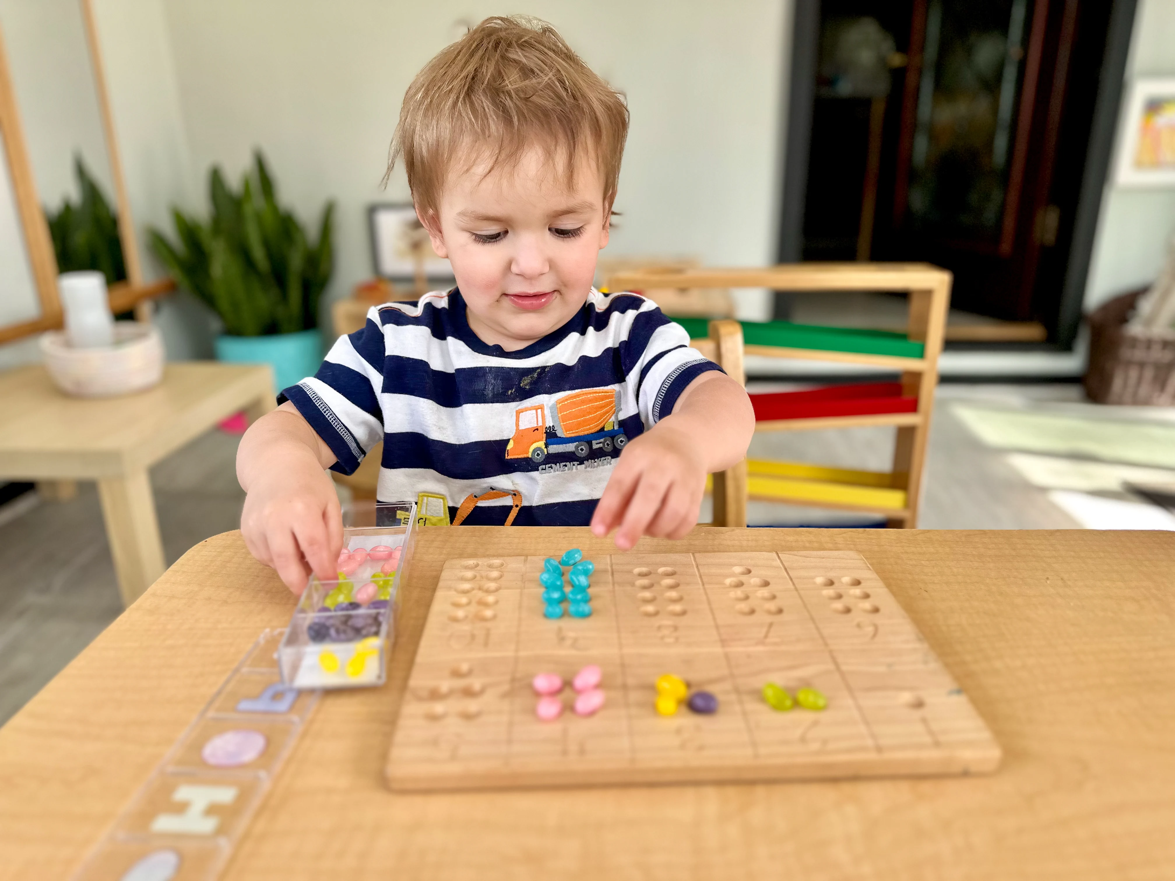 Montessori toddler uses wooden board to count jelly beans as he learns numbers in his Montessori playroom