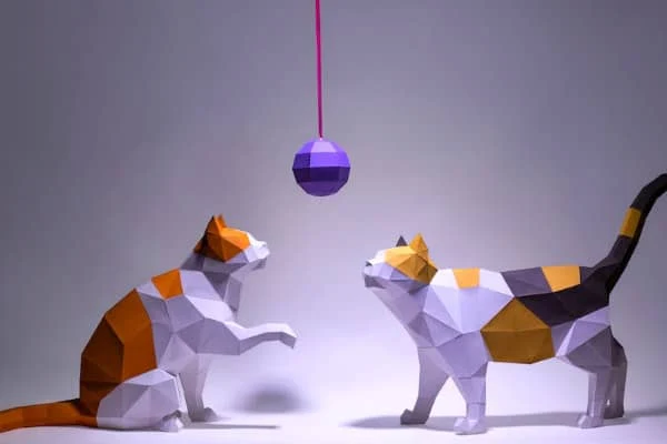 two lowpoly paper cats looking up at lowpoly ball dangling on string