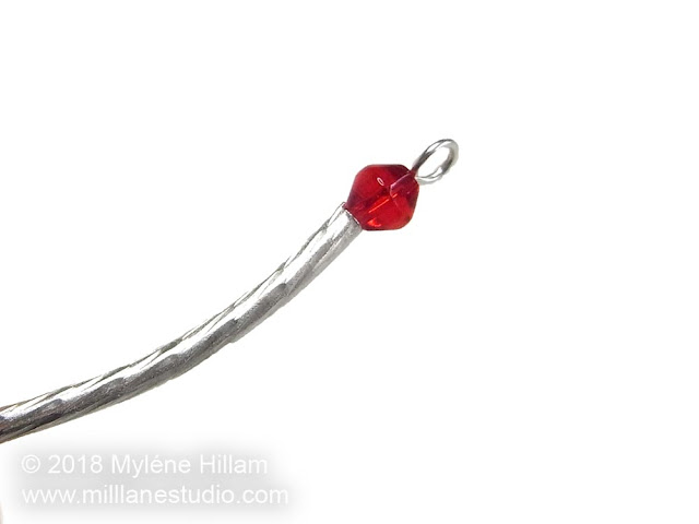 Eye pin strung with twisted silver tube and red bicone.