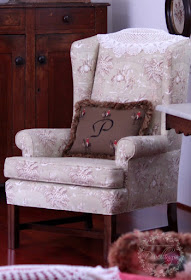 The camelback chair is upholstered in a hunt scene toile with an emroidered pillow.