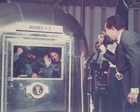 A photograph of Nixon exchanging "OK" gestures with crew members behind glass. 