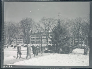 Black and white photo of college students walking to class on the green in the snow with the christmas tree in the background