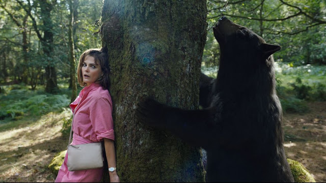 A woman in pink and a bear stand on opposite sides of a tree