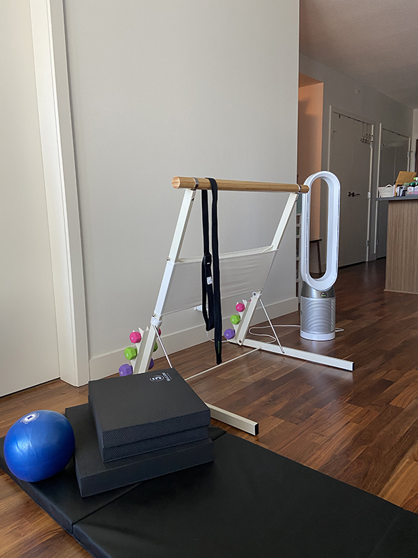 At-home barre workout setup featuring Bootykicker portable barre, Dyson fan, tri-fold exercise mat, foam physio mats, pilates ball, dumbbells, and yoga strap