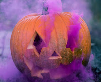 Close up photo of a jack o lantern or carved pumpkin with weird purple smoke emanating from its eyes etc