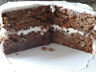 A Zucchini Carrot Pineapple Cake with Walnuts and Cream Cheese Frosting sliced in half on a white cake plate.