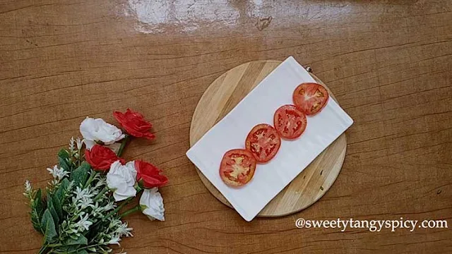 A clean and spacious serving plate showcasing a beautiful arrangement of ripe red tomato slices. The tomatoes are carefully layered in either a circular or linear pattern, creating an inviting canvas for the rest of the Caprese salad ingredients. This thoughtful presentation sets the stage for a visually captivating and appetizing dish, perfect for a delightful dining experience.