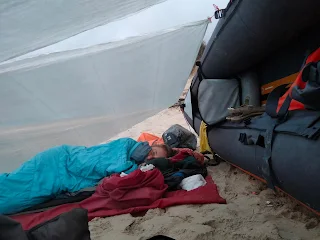 Murielle lies in her sleeping bag on her isolation mat under a tarp that is fixed at the boat