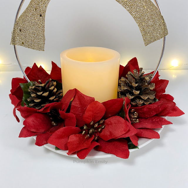 A close up of red flowers, pinecones, and a LED candle on a Christmas hoop centerpiece.