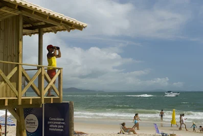 Guardavidas vigilando desde el balcón de su guarita. Playa de Jurerê con gente divirtiéndose en la arena.