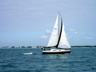 A red sailboat is moving smartly along on a blue ocean.  It is towing a dinghy behind it.