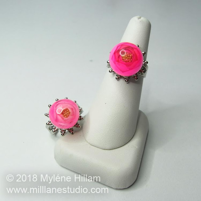 Two UV Resin rose rings, one light pink and one dark pink, displayed on a white ring cone.
