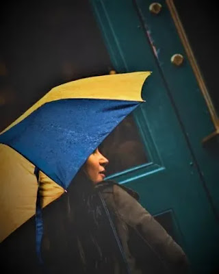 A girl with the yellow umbrella at the door of a house