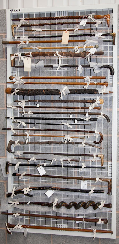 A series of walking sticks and canes mounted on wire mesh