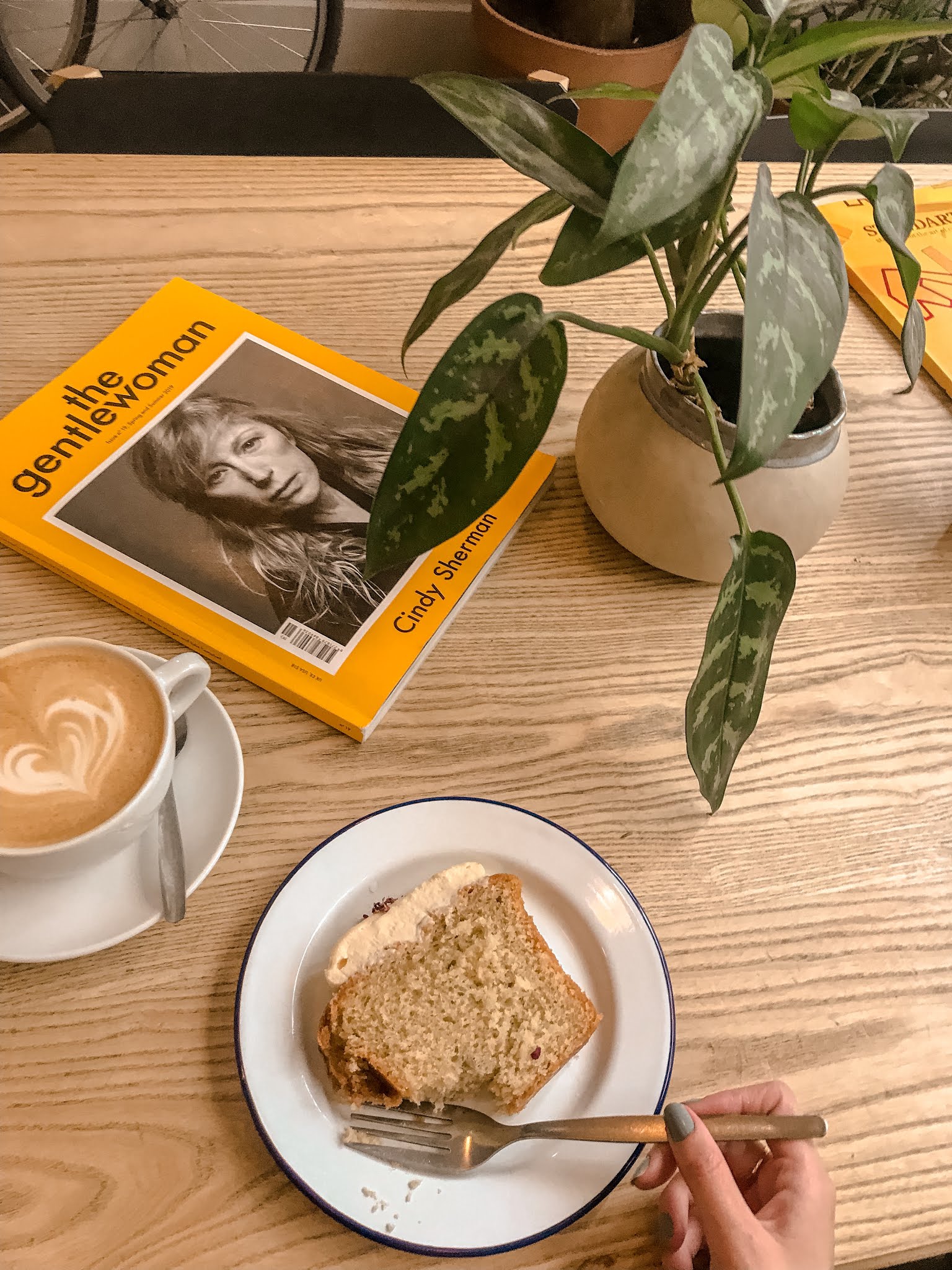 flatlay from coffee shop of the gentlewoman magazine, latte art, plant, and piece of cake