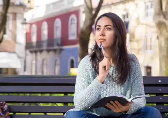 Mulher relaxando no parque enquanto pratica autocuidado.