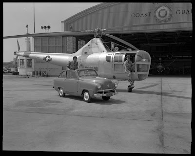 Man stands in a car in front of a helicopter