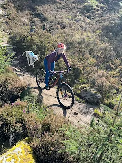 women riding bike down scottish highland mountain with dog