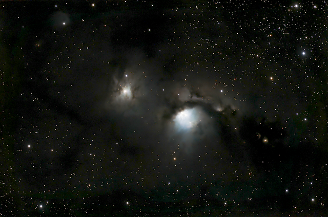 A telescopic image of stars showing two bright areas that are embedded in blue-white and black clouds.
