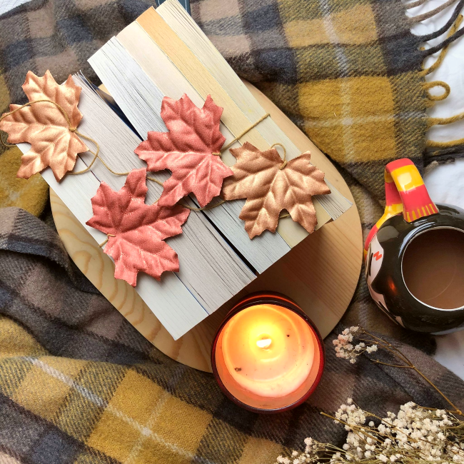 Books next to each with spines facing down and fake autumn leaves on top, next to a lit candle