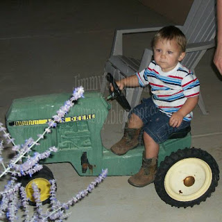 Grandson Benjamin sitting on a toy John Deere tractor wearing his cowboy boots