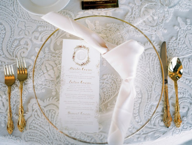 gold rimmed glass charger with knot napkin fold and gold flatware