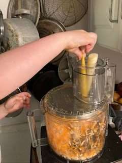 kid hand adding carrots to a cuisinart for shredding